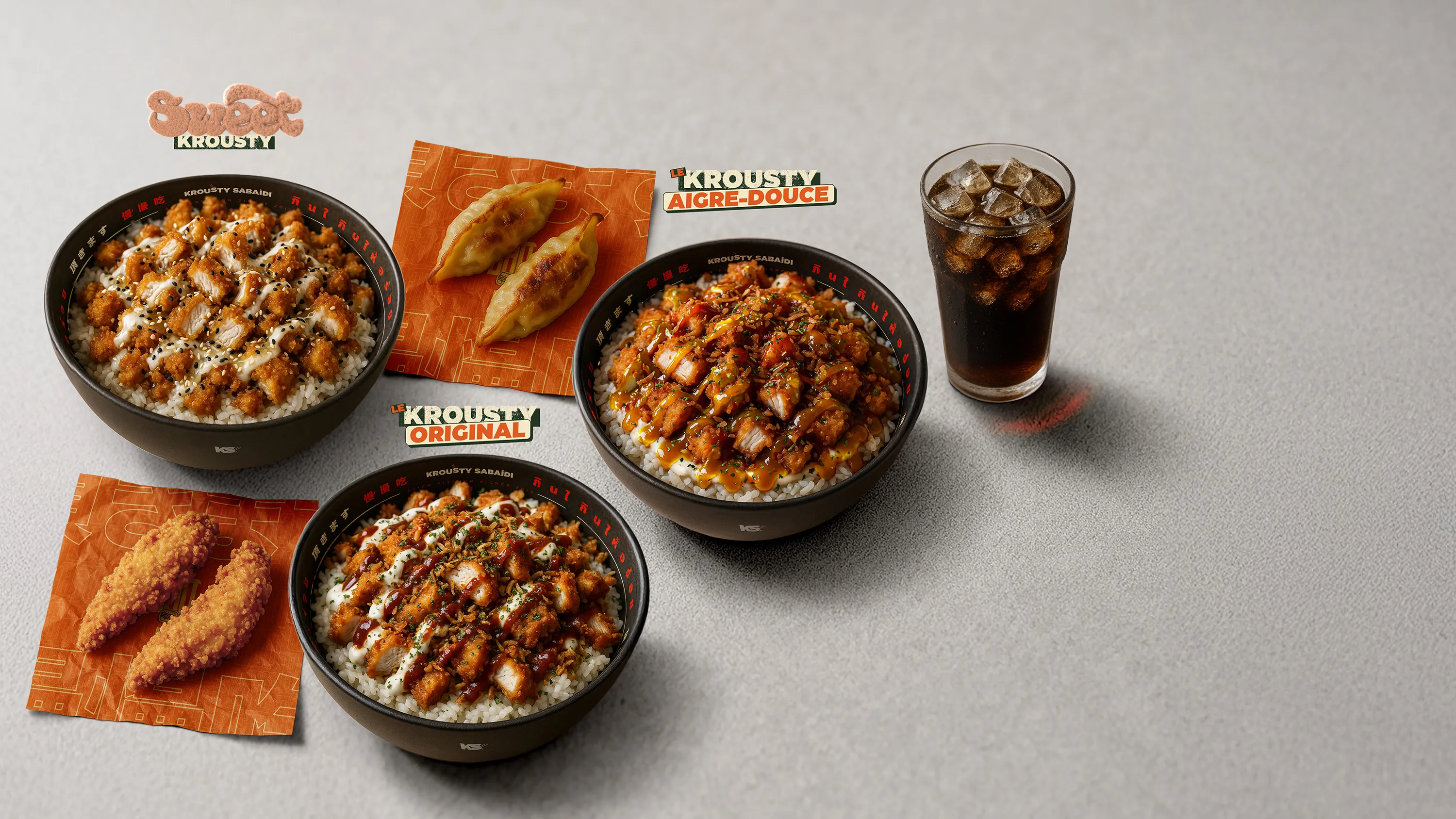 Trois bols de riz garnis de poulet pané Krousty avec sauce, accompagnés de nuggets de poulet et d'un verre de soda glacé sur un fond gris.