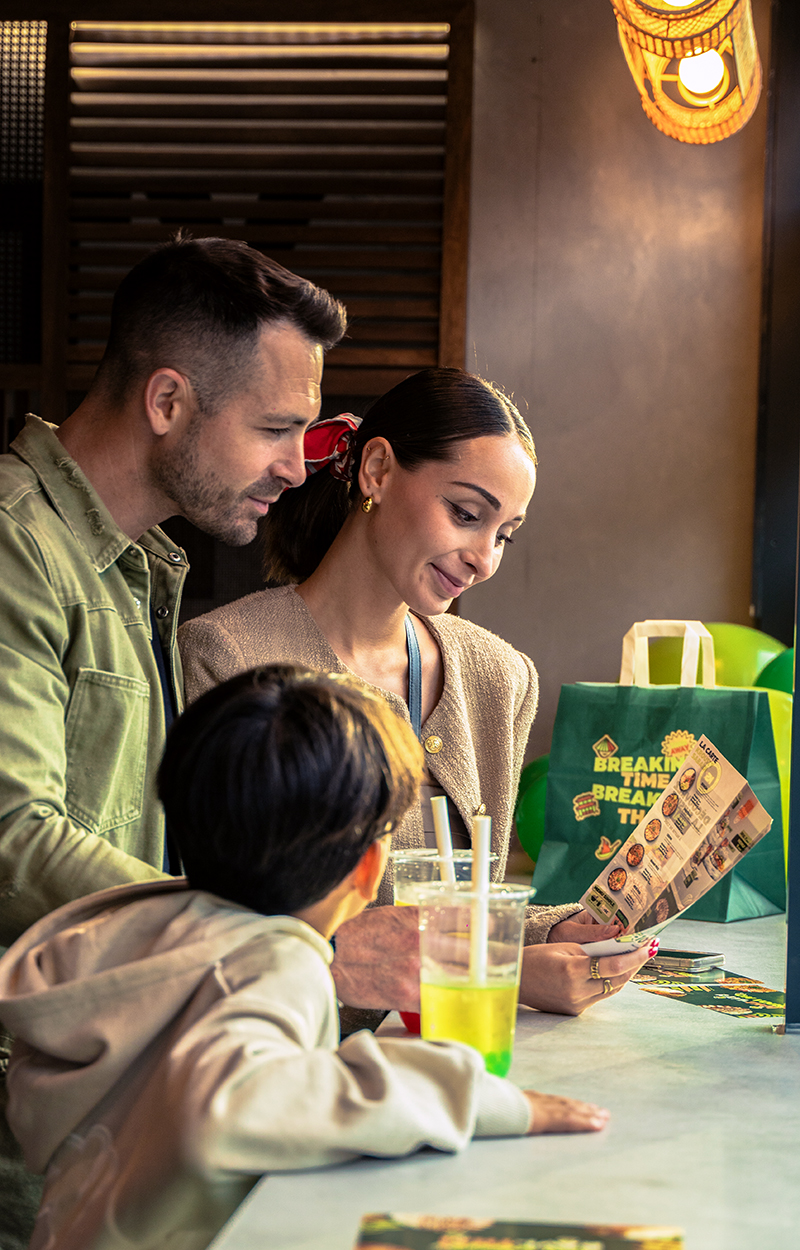 Famille, avec parents et enfant, choisissant des plats sur un menu dans un restaurant de cuisine asiatique. Une photo d'un client dans l'établissement Krousty Sabaïdi avec sa famille.