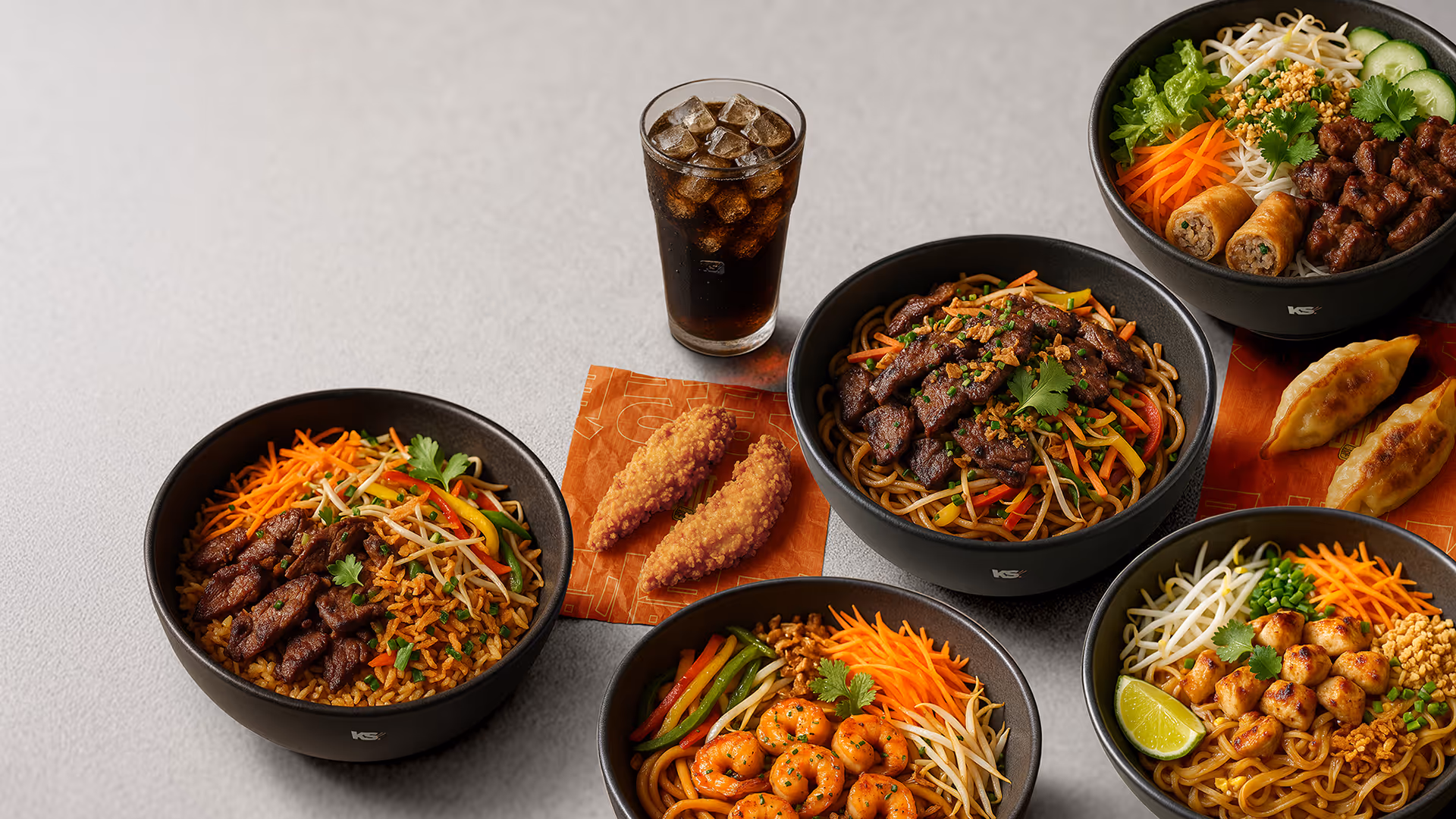 Assortiment de plats asiatiques dans des bols noirs : nouilles sautées au bœuf, crevettes, salade vietnamienne avec nems, accompagnés de gyoza et d'un soda glacé.