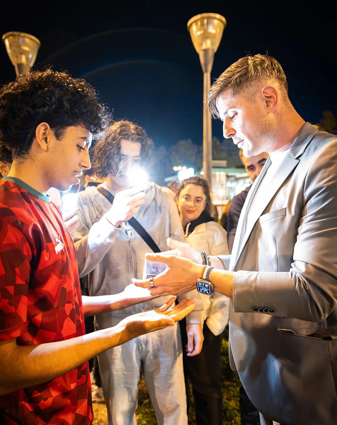 Homme en costume gris signant des autographes pour des fans dans une rue la nuit, éclairage urbain en arrière-plan.