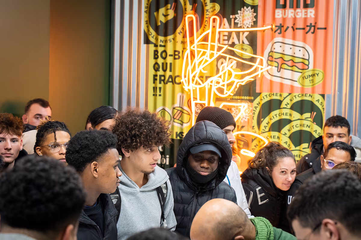 Groupe de clients attendant devant un restaurant Krousty Sabaïdi avec signalétique néon et illustrations murales de nourriture.