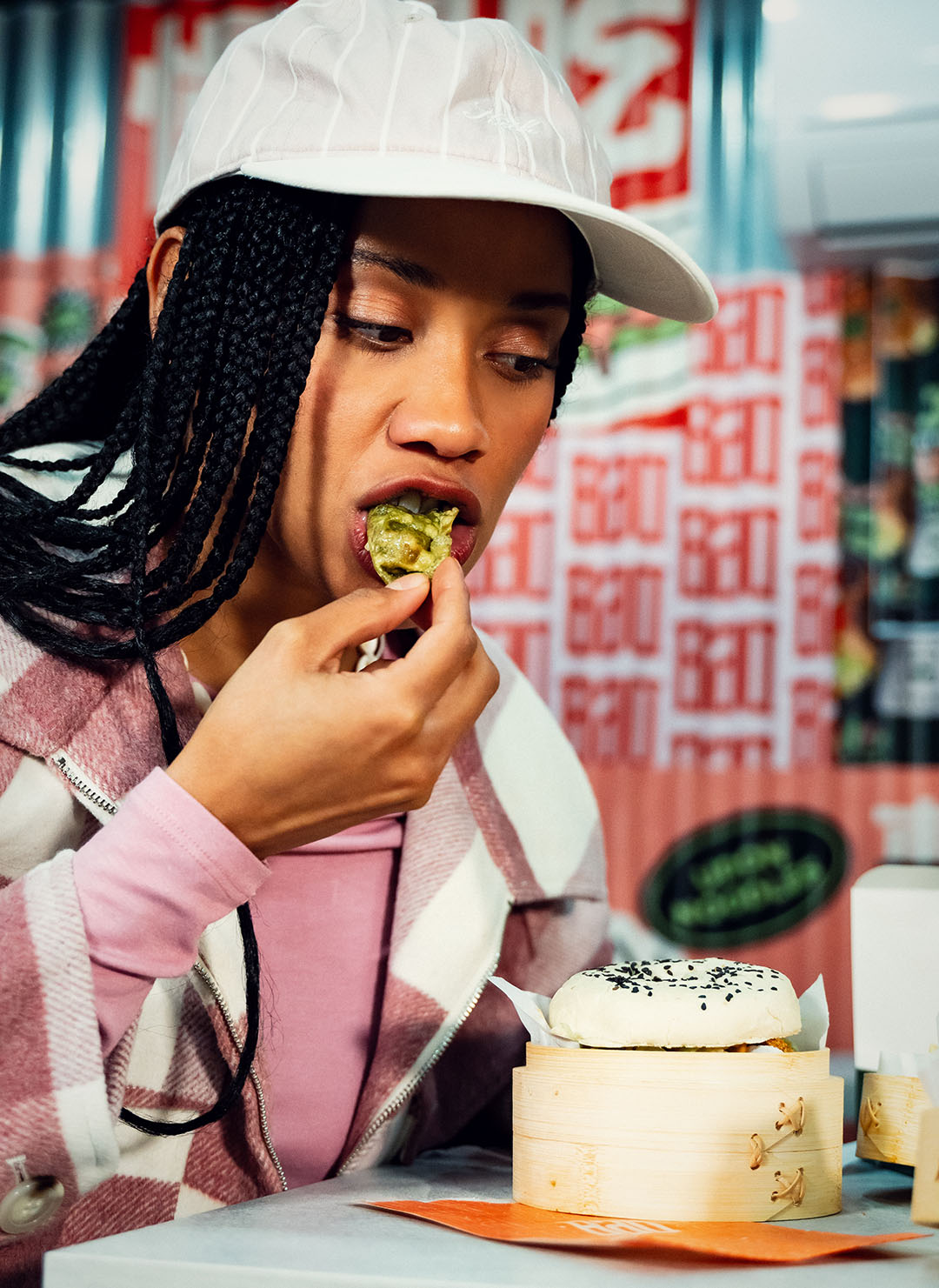 Femme mangeant un gyoza dans un restaurant asiatique Crousty Sabaïdi, avec en premier plan un bao au poulet croustillant, street food asiatique moderne, décor urbain coloré.