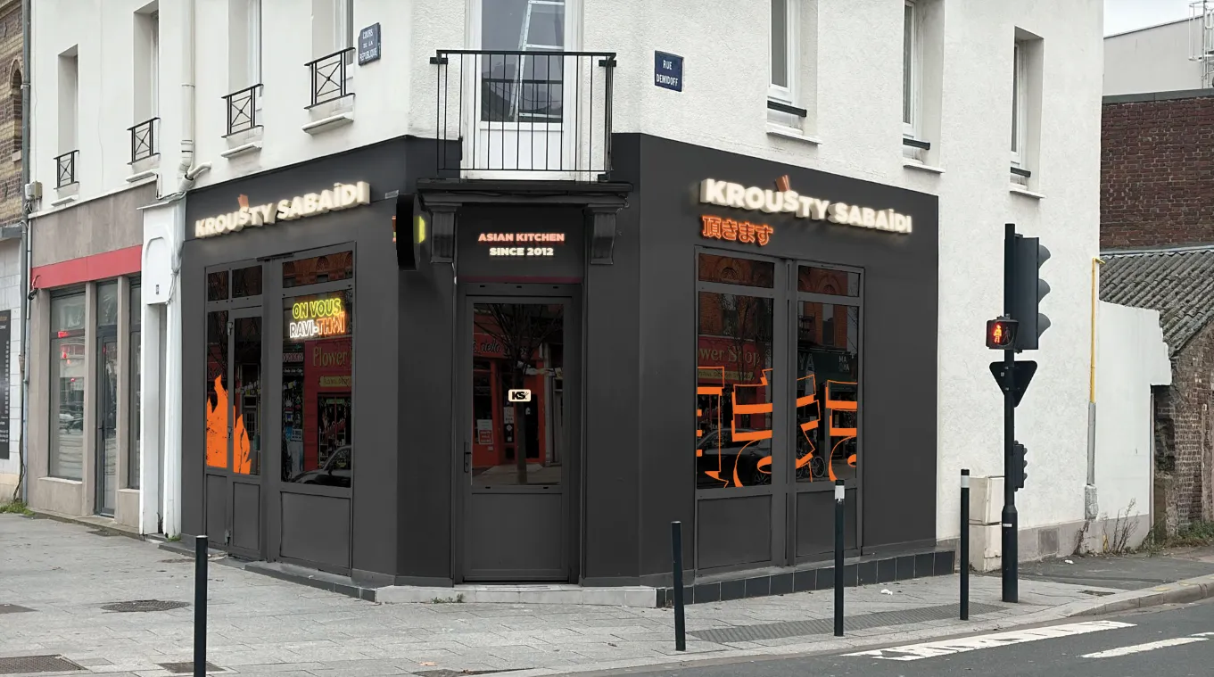 Façade d’angle du restaurant Krousty Sabaïdi au Havre, devanture noire avec enseignes « KROUSTY SABAÏDI » et « ASIAN KITCHEN SINCE 2012 », vitrines donnant sur des sièges orange, passage piéton et feu tricolore au premier plan.